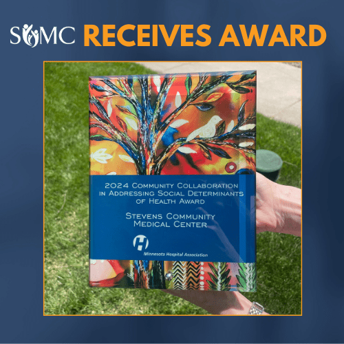 A hand holds a colorful award plaque titled “2024 Community Collaboration in Addressing Social Determinants of Health Award” for Stevens Community Medical Center (SCMC), recognizing their commitment and achievement.