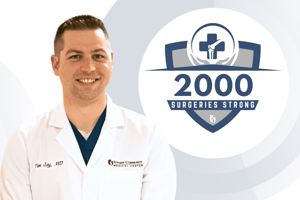 A smiling doctor in a white coat stands beside a badge reading “2000 Surgeries Strong” with a medical cross and laurel wreath, celebrating a milestone achievement in surgical procedures and showcasing exceptional medical expertise.
