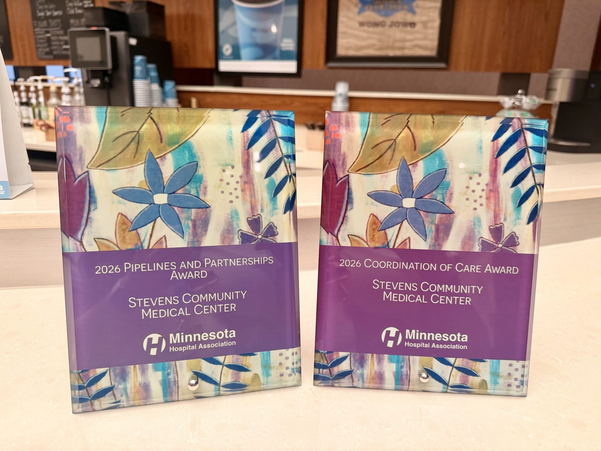 Two colorful awards from the Minnesota Hospital Association (MHA Conference) for Stevens Community Medical Center (SCMC), labeled “2026 Pipelines and Partnerships Award” and “2026 Coordination of Care Award,” proudly displayed on a counter.